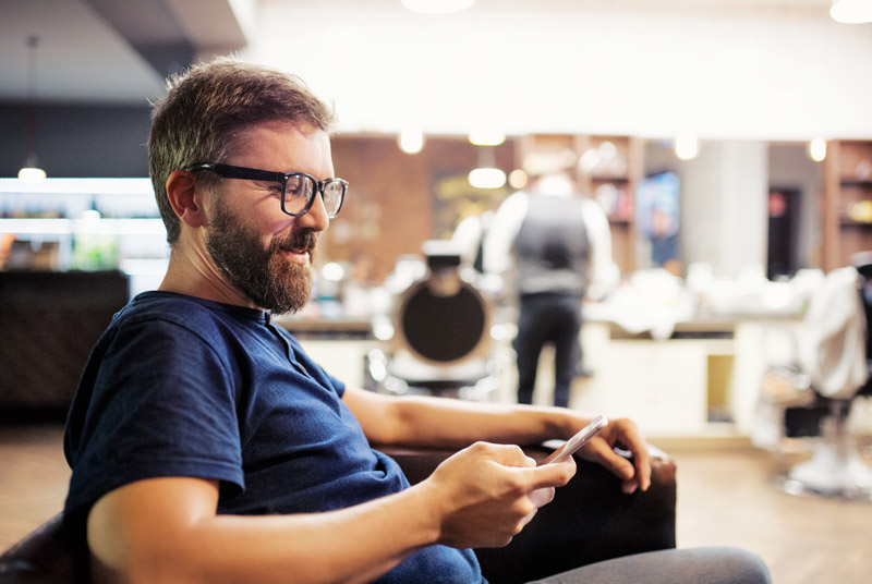 A middle-aged man wearing reading glasses looking at his phone