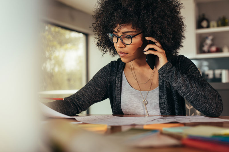A woman with glasses on the phone, checking if her health insurance covers laser eye surgery
