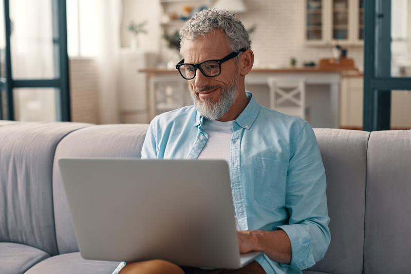 A mature man with glasses, looking at his laptop and reading about the reasons people opt for laser cataract surgery