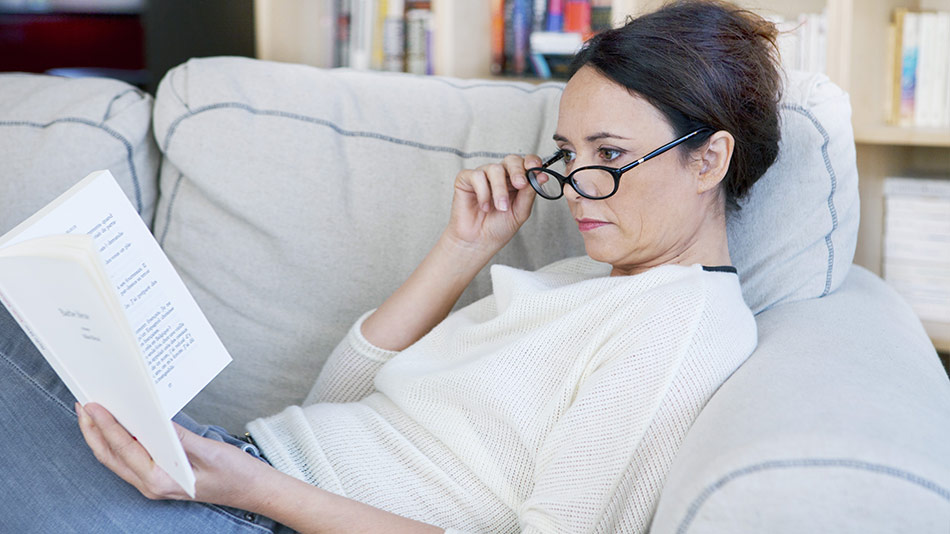 Middle-aged woman with reading glasses struggling to read a book due to her presbyopia