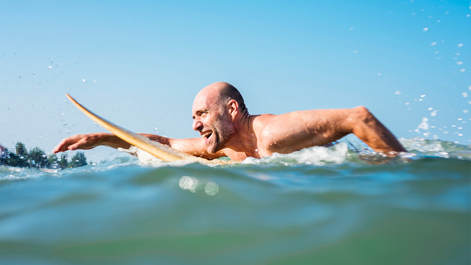 Elderly man relishing the summer season as he swims and surfs in the ocean, liberated from glasses and contact lenses.