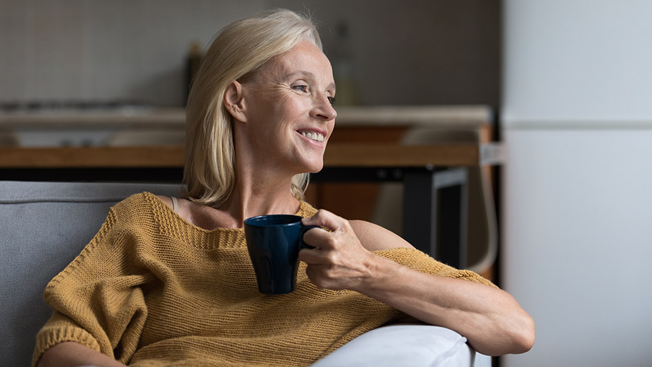 Senior woman holding a coffee cup, looking out the window and smiling