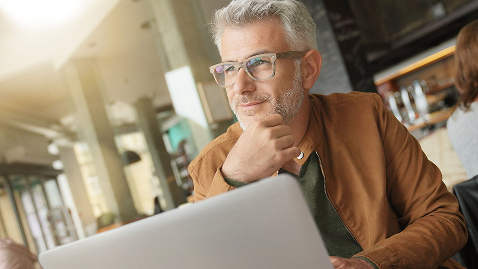 A senior man wearing reading glasses in a cafe, thinking about the possibility of getting lens replacement surgery