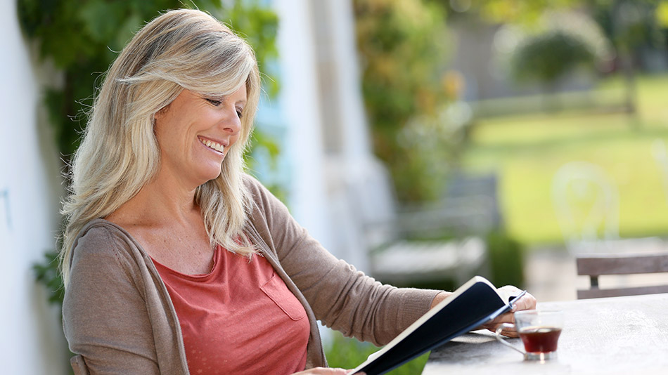 Senior woman enjoying reading without glasses in her garden after lens replacement surgery.