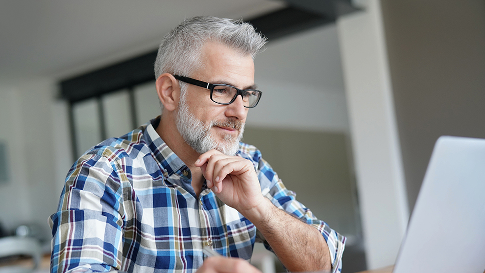 Middle-aged man with glasses, searching on laptop to determine if lens replacement surgery can correct astigmatism
