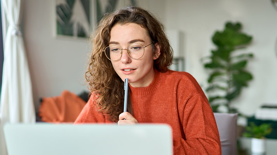 A woman with glasses holding a pen and looking at her laptop, thinking about how much ICL surgery costs.