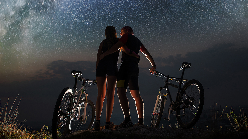 Two bikers gazing at the stars in the night sky while on a mountain
