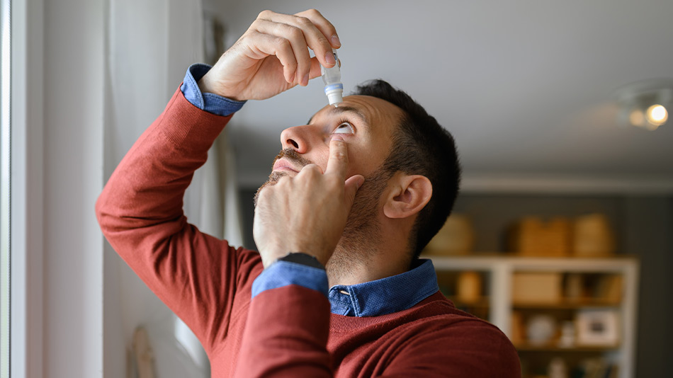 A young man putting in eye drops to help with his dry eyes.