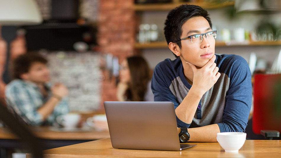 A young man with glasses sitting in a coffee shop, thinking about getting LASIK eye surgery, but he has keratoconus.