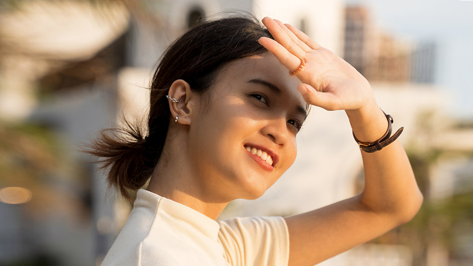 A woman raising her hand to cover her eye from the bright sunlight.