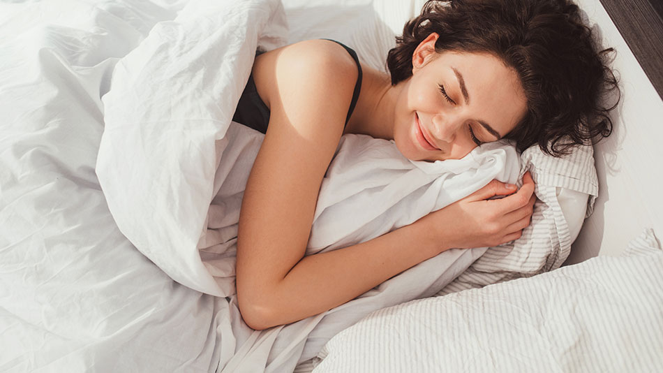 A beautiful woman lying on a bed, smiling because she had a great sleep last night.
