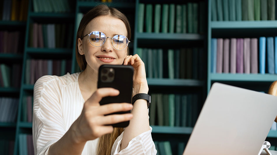 A young beautiful woman with glasses looks at her phone.