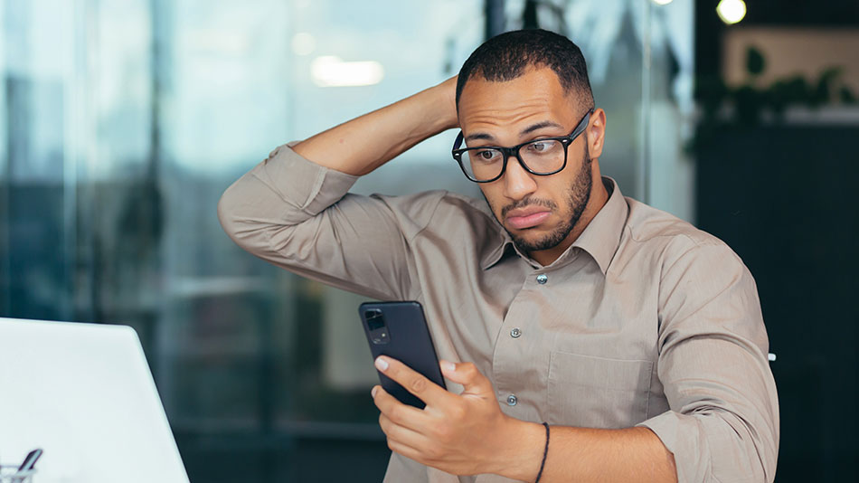 A man with glasses looks surprised while glancing at his phone.