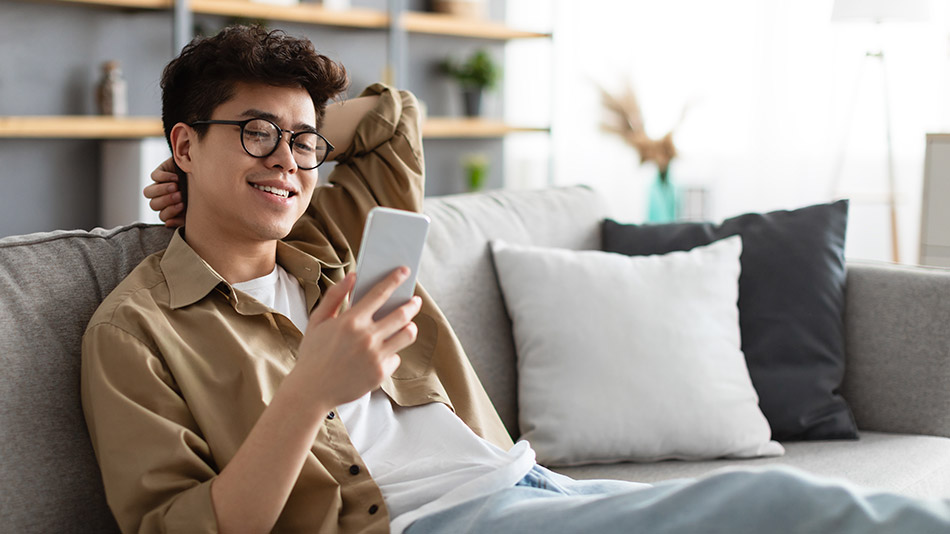 A young Asian man uses his phone on the sofa.