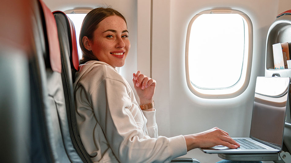 A calm woman sits by an airplane window, smiling at the camera