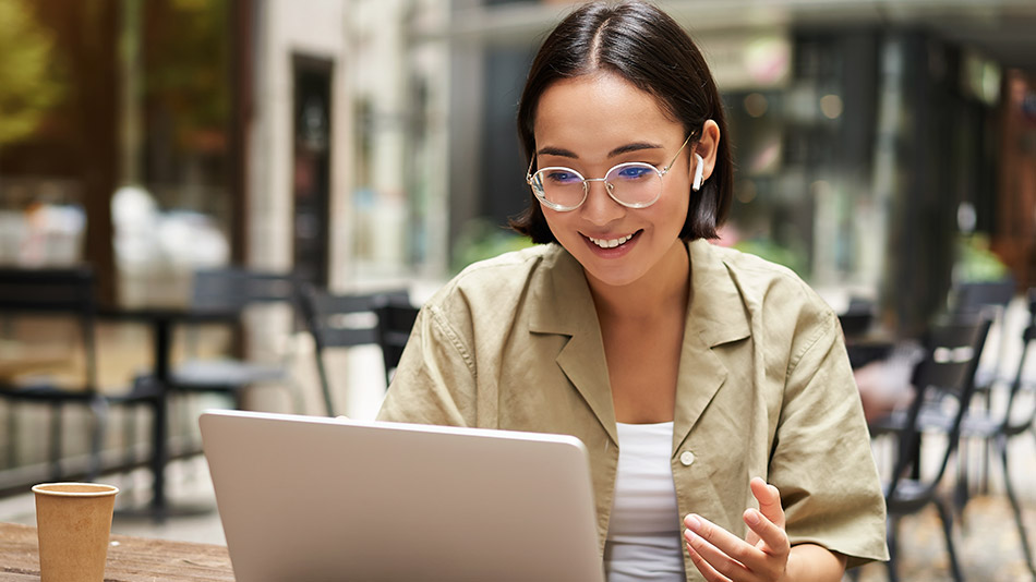 A young woman wearing glasses reads an article on her laptop.