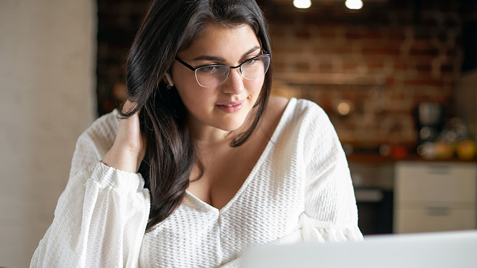 A slightly overweight young woman uses a laptop.