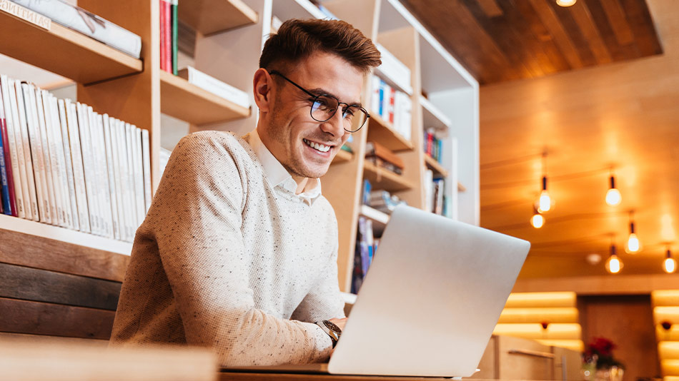 A young, handsome man with glasses is using a laptop in a cafe.
