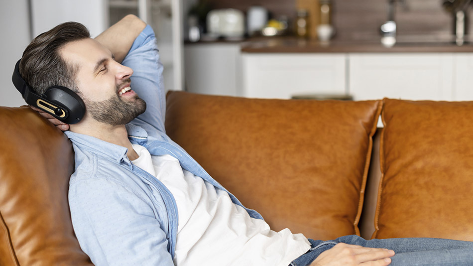 A young man relaxing on a couch, listening to music.