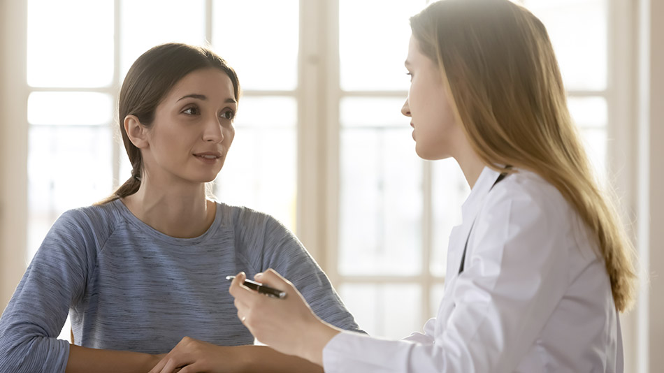A young woman wearing a long-sleeve shirt having an eye consultation with a female doctor.