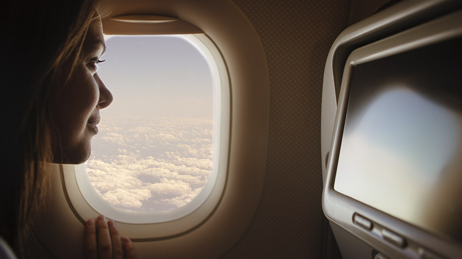 A beautiful young woman looking out of an airplane window.