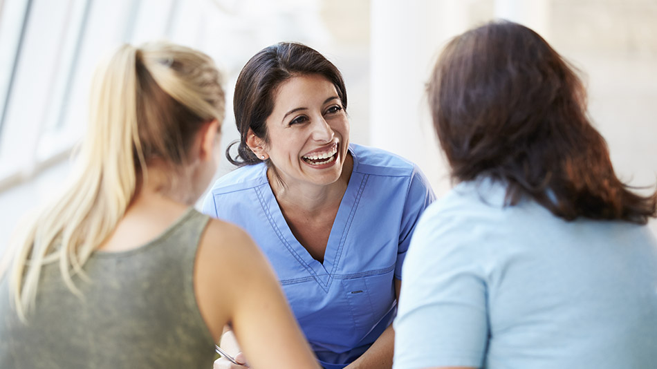 An ecstatic woman in blue scrubs having a consultation with two women in front of her.