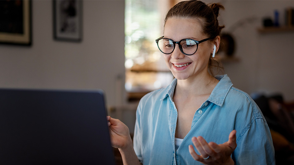 A young woman with glasses is sitting and pondering while looking at her laptop.